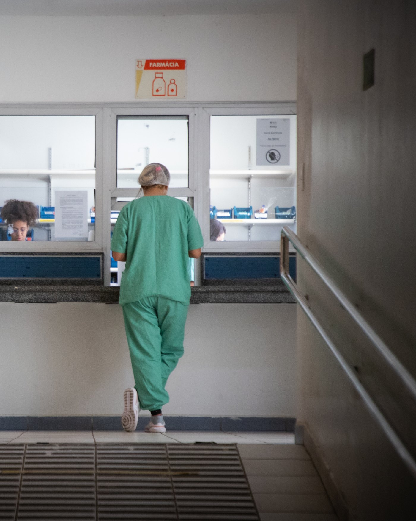 Profissional de saúde de uniforme verde na janela da farmácia de um hospital