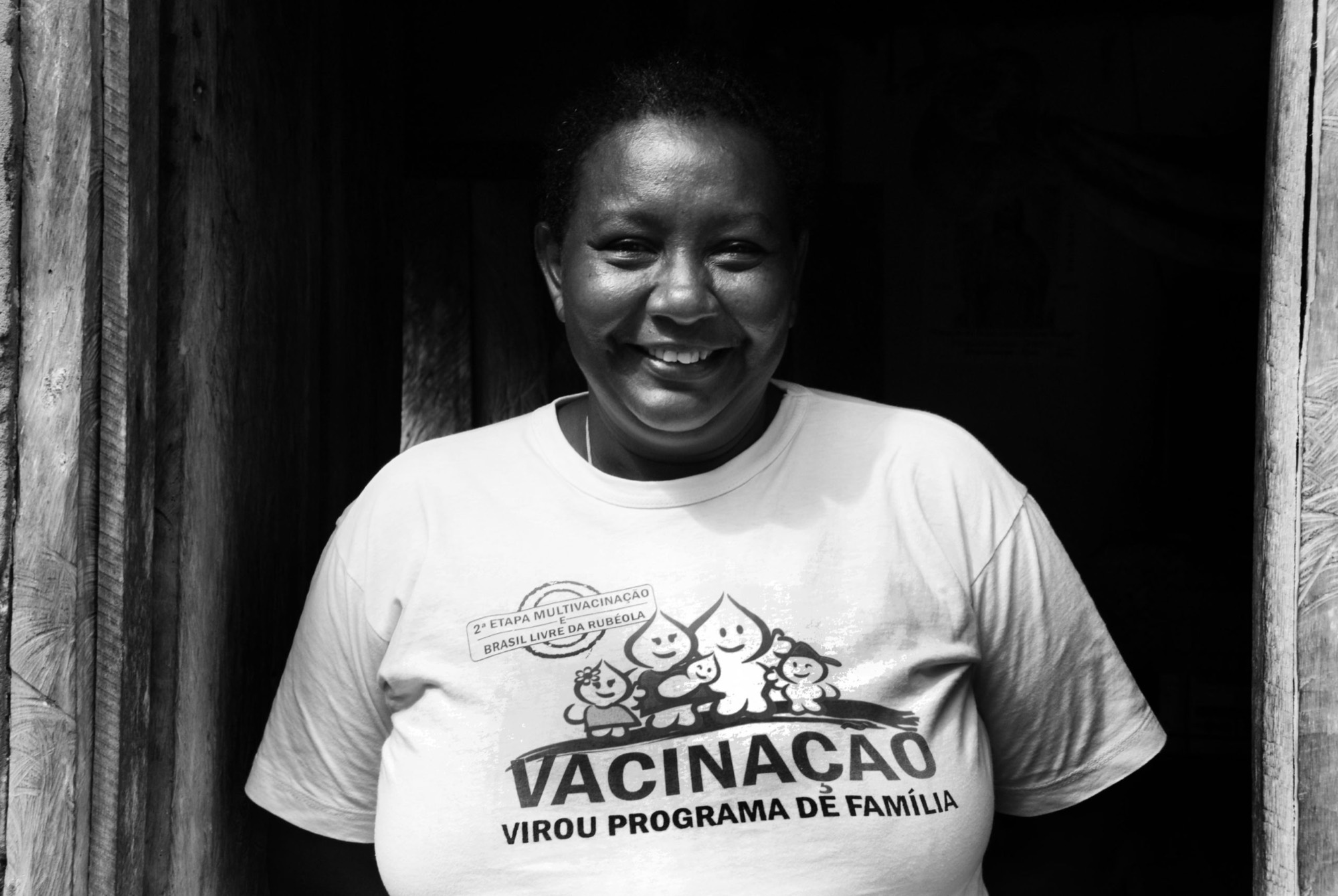 Agente comunitária de saúde sorrindo no vão da porta de uma casa