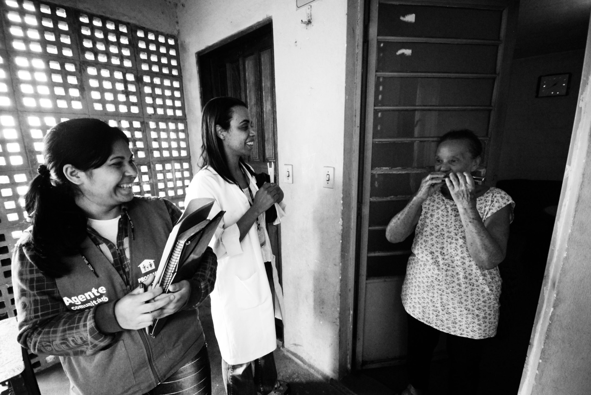 Agente comunitária, enfermeira e moradora conversam na porta de uma casa
